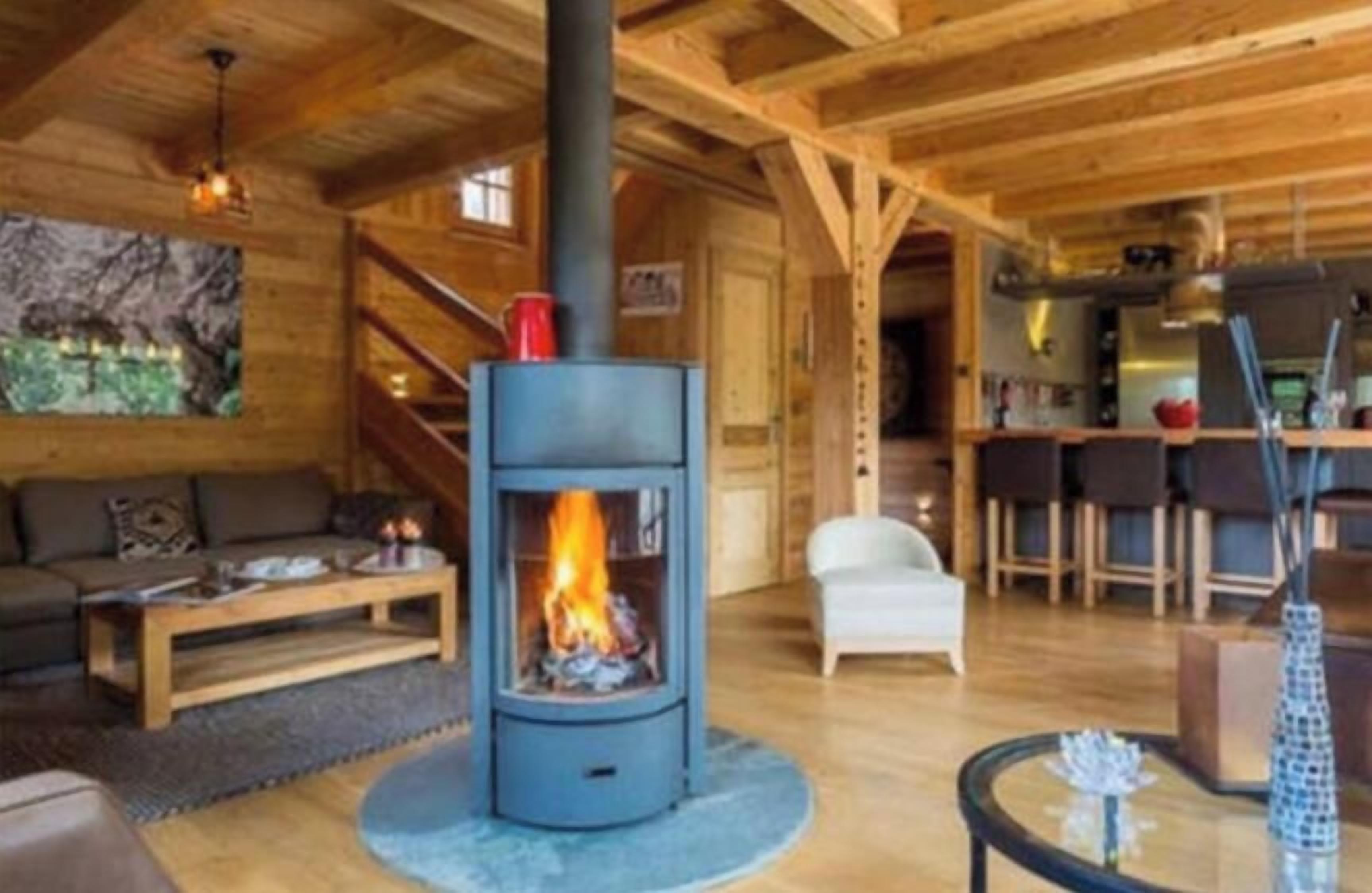 A cozy living room with a central wood-burning stove, a sofa, a coffee table, and a dining area with bar stools.