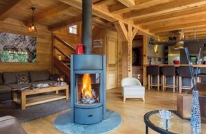 Un salon chaleureux avec un poêle à bois central, un canapé, une table basse et un coin repas équipé de tabourets de bar.