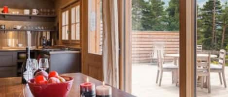 A wooden interior with a kitchen and dining area, large windows, and a view of a deck and trees.