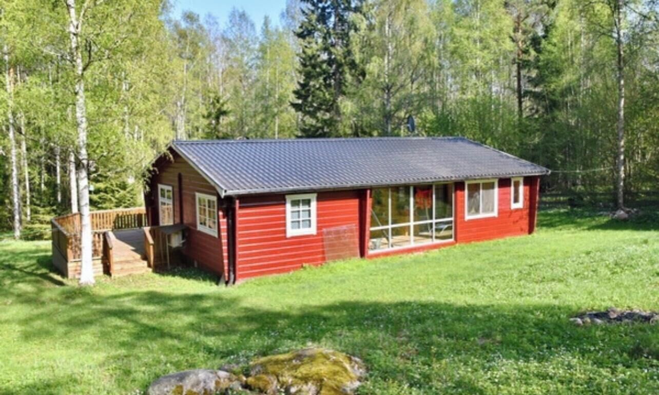 A red cabin with a dark roof, surrounded by a grassy area and trees.