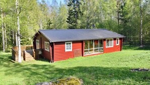 A red cabin with a dark roof, surrounded by a grassy area and trees. - Exclusive lake house in Småland | Private boat, fireplace & absolute tranquillity (Aggatorp)