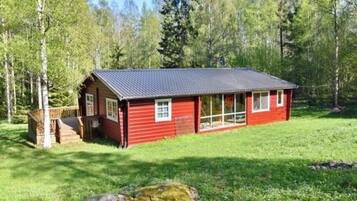 A red cabin with a dark roof, surrounded by a grassy area and trees.