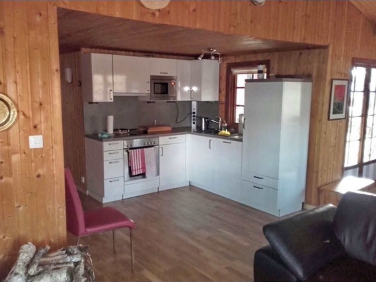 A compact kitchen with white cabinets, a microwave, and a refrigerator. There is a pink chair and a black leather chair.