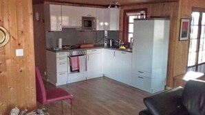 A compact kitchen with white cabinets, a microwave, and a refrigerator. There is a pink chair and a black leather chair. - Exclusive lake house in Småland | Private boat, fireplace & absolute tranquillity (Aggatorp)
