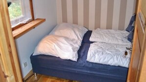 A small, single-bed room with a striped headboard, a window with a wooden shelf, and a wooden floor. - Exclusive lake house in Småland | Private boat, fireplace & absolute tranquillity (Aggatorp)