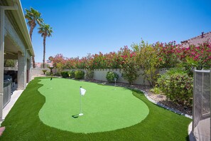 A well-maintained artificial green golf course with two flags, surrounded by lush landscaping and palm trees.