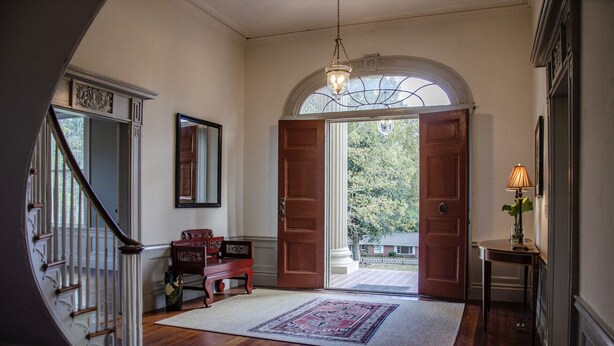 A grand entrance with a wooden staircase, a rug, a bench, and a lamp. - Historic Rockwell House (Milledgeville)