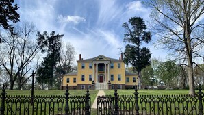 A large yellow building with a symmetrical facade, surrounded by a well-maintained lawn and a decorative iron fence. - Historic Rockwell House (Milledgeville)