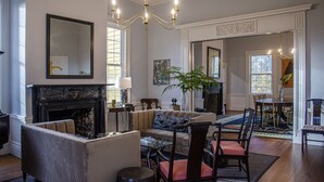 A spacious living room with a fireplace, comfortable seating, a dining area, and a large window providing natural light. - Historic Rockwell House (Milledgeville)