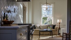 A modern kitchen with a herringbone backsplash, a built-in stove, and a dining area with a sofa and coffee table. - Historic Rockwell House (Milledgeville)