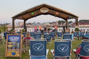 Un escenario techado al aire libre con un cartel que dice "Cedar Hammock Brewery Stage" y un letrero que anuncia "Música en vivo todas las noches" a partir de las 7 pm.