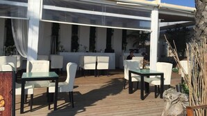 An outdoor seating area with white chairs and tables, covered by a white canopy.