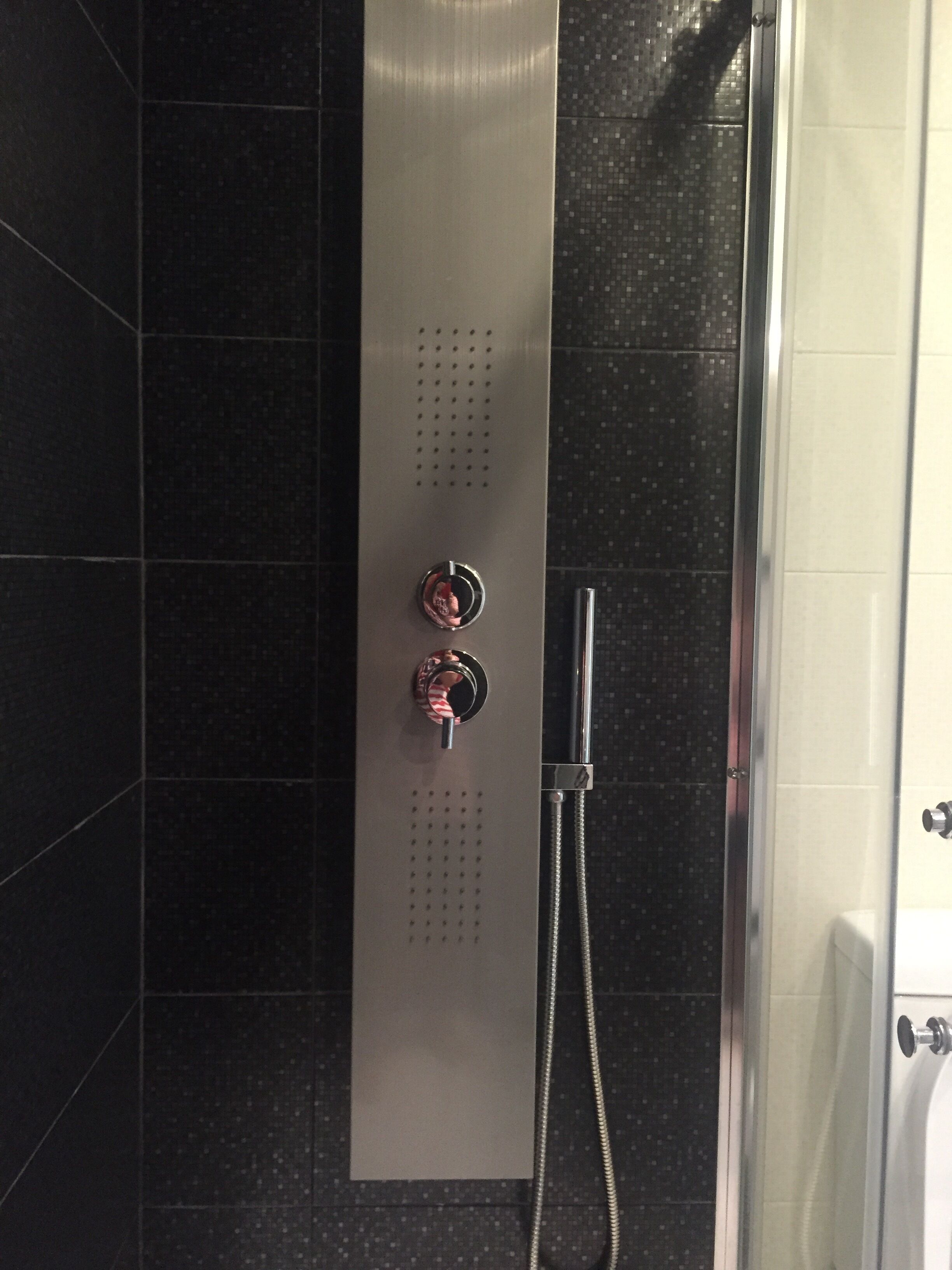 Eine Dusche mit Handbrause und Bedienfeld an der Wand.