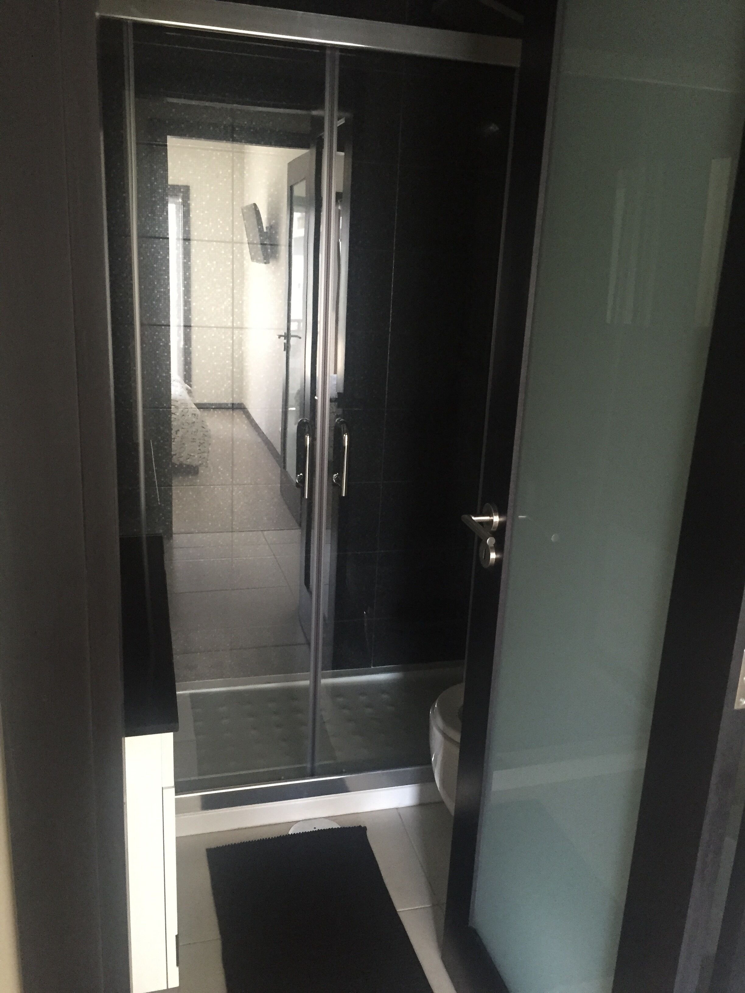 Une salle de bain moderne avec une douche à parois de verre, des toilettes et un tapis de sol foncé.
