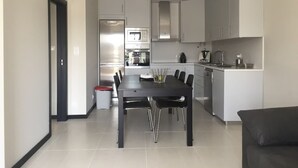 A modern kitchen with a dining area, featuring a central island, built-in appliances, and a dark dining table.