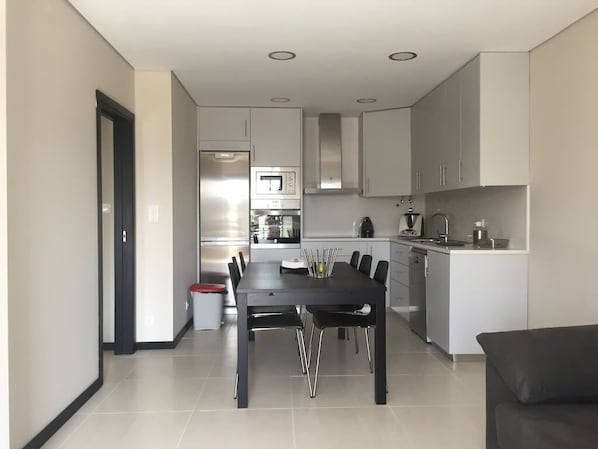 Una cocina moderna con comedor, que incluye una isla central, electrodomésticos integrados y una mesa de comedor oscura.