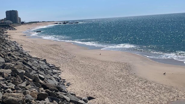 A beach with a rocky shoreline, clear blue water, and a distant building.
