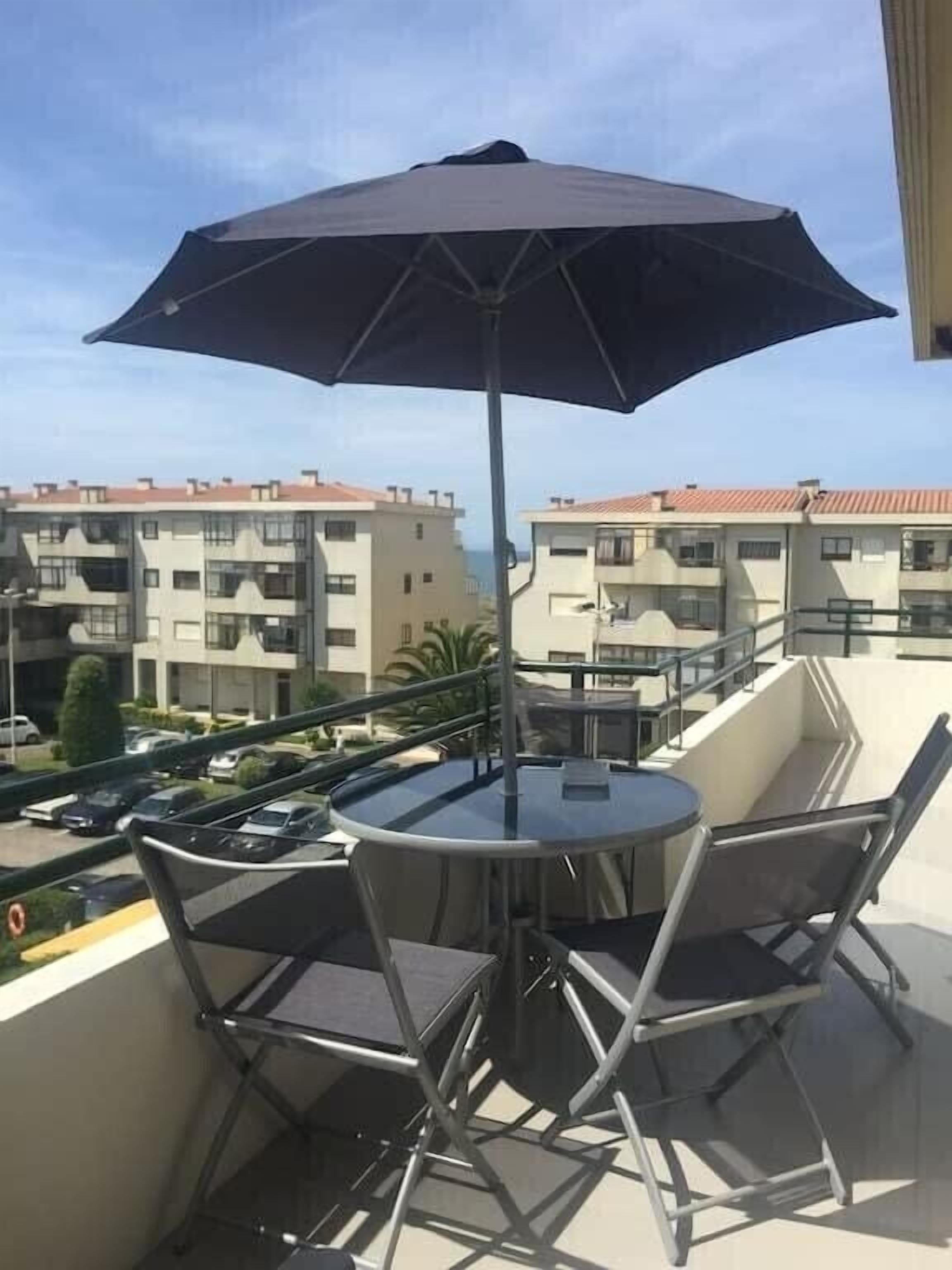Un balcon avec une table et des chaises, un parasol et une vue sur des immeubles d’habitation.