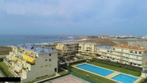 A residential complex with multiple apartment buildings, a swimming pool, and a view of the sea.