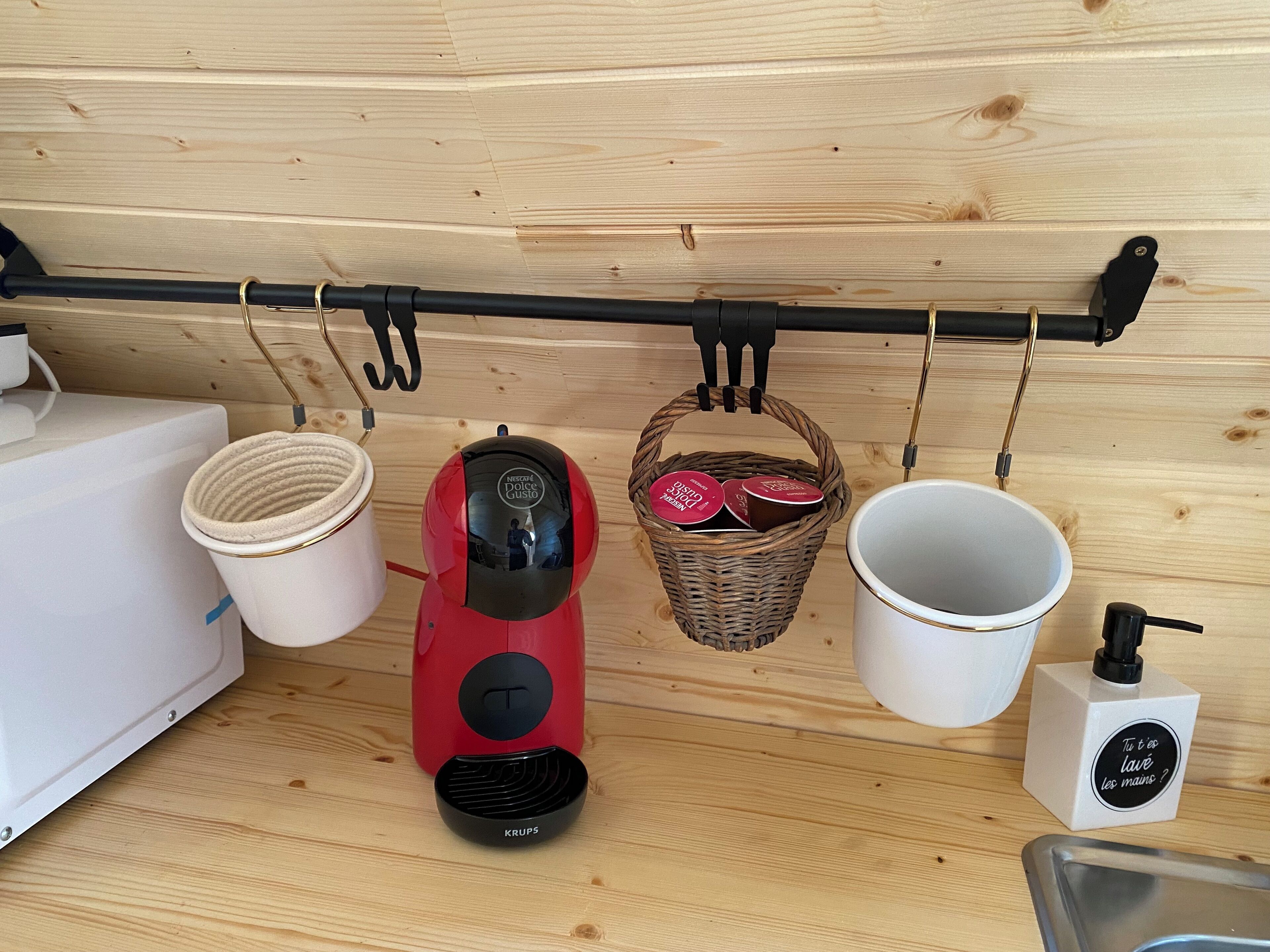 A kitchen with a coffee machine, a basket with containers, a white mug, and a soap dispenser.