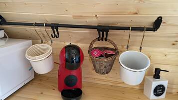 A kitchen with a coffee machine, a basket with containers, a white mug, and a soap dispenser.