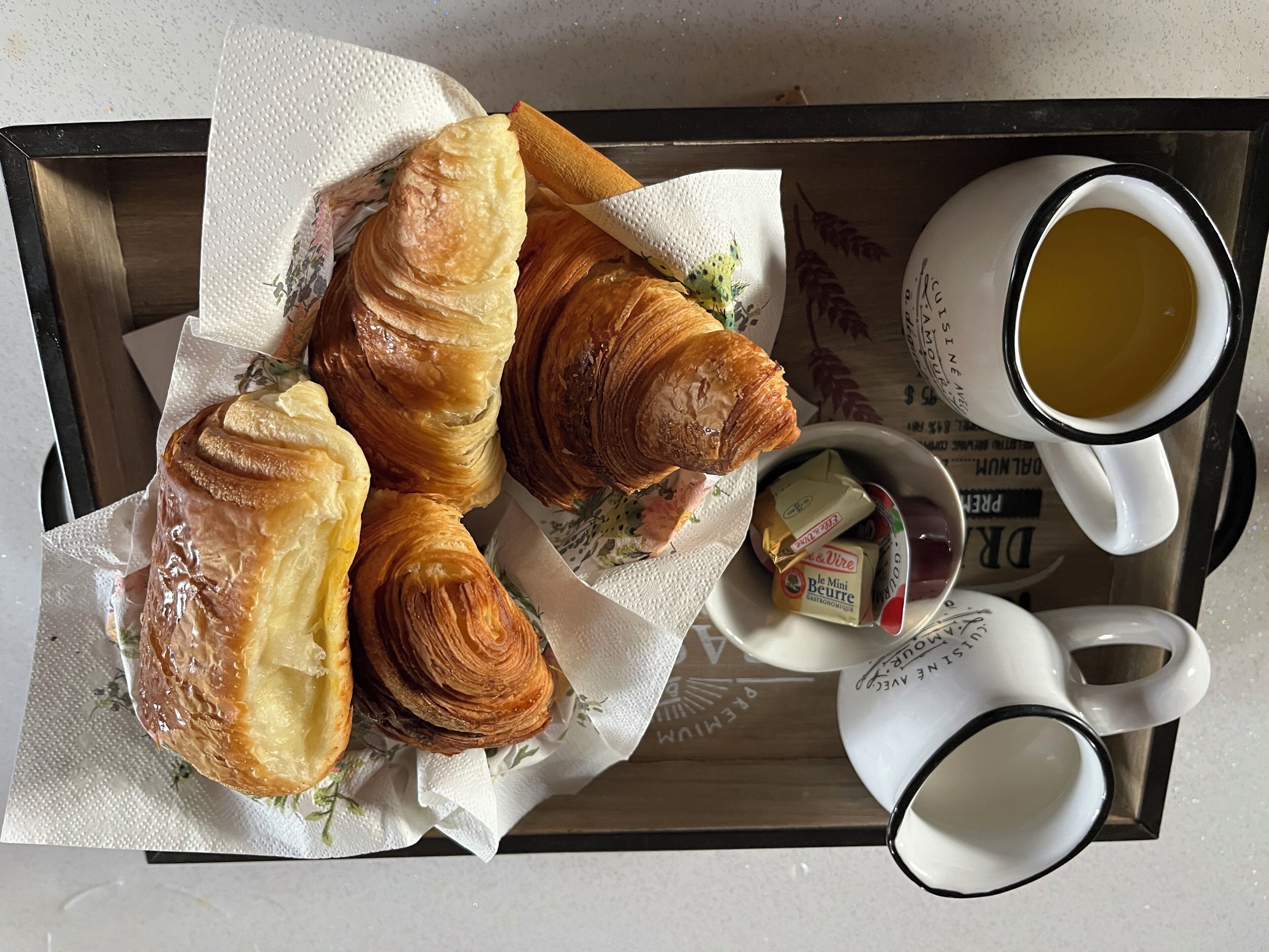 A tray with croissants, butter, and coffee cups.