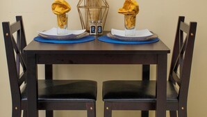 A dining table with two chairs, a framed painting above, and salt and pepper shakers on the table.