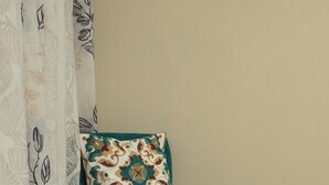 A teal upholstered chair with a patterned cushion, a matching ottoman, and a patterned curtain in a room with a plain wall and a tiled floor.