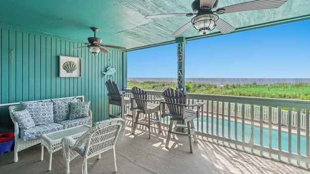 A covered outdoor seating area with a view of the beach, a ceiling fan, and a table with chairs. - Windcrest Villas 105-2BR/2BA Oceanfront Condo in Windy Hill (North Myrtle Beach)