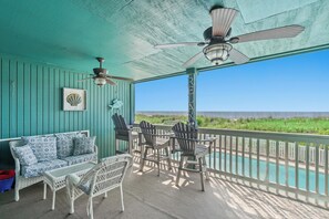 Uma área de estar coberta ao ar livre com vista para a praia, um ventilador de teto e uma mesa com cadeiras.