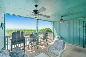 A covered outdoor area with ceiling fans, Adirondack chairs, wicker furniture, and a view of the ocean.