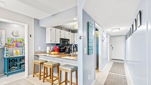 A modern kitchen with white cabinets, a central island with stools, a microwave, and a coffee maker. - Windcrest Villas 105-2BR/2BA Oceanfront Condo in Windy Hill (North Myrtle Beach)