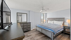 A bedroom with a bed, dresser, mirror, ceiling fan, and nightstand.