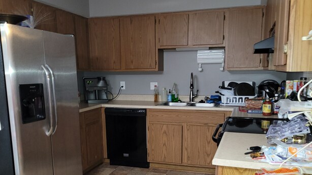 A compact kitchen with wooden cabinets, a stainless steel refrigerator, a dishwasher, and a cluttered countertop with various items. - Private condo sleeps up to 4 with private hot tub (Lincoln)