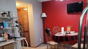 A compact kitchen with a dining area, featuring a red wall, a TV mounted above the table, and a chandelier. - Private condo sleeps up to 4 with private hot tub (Lincoln)