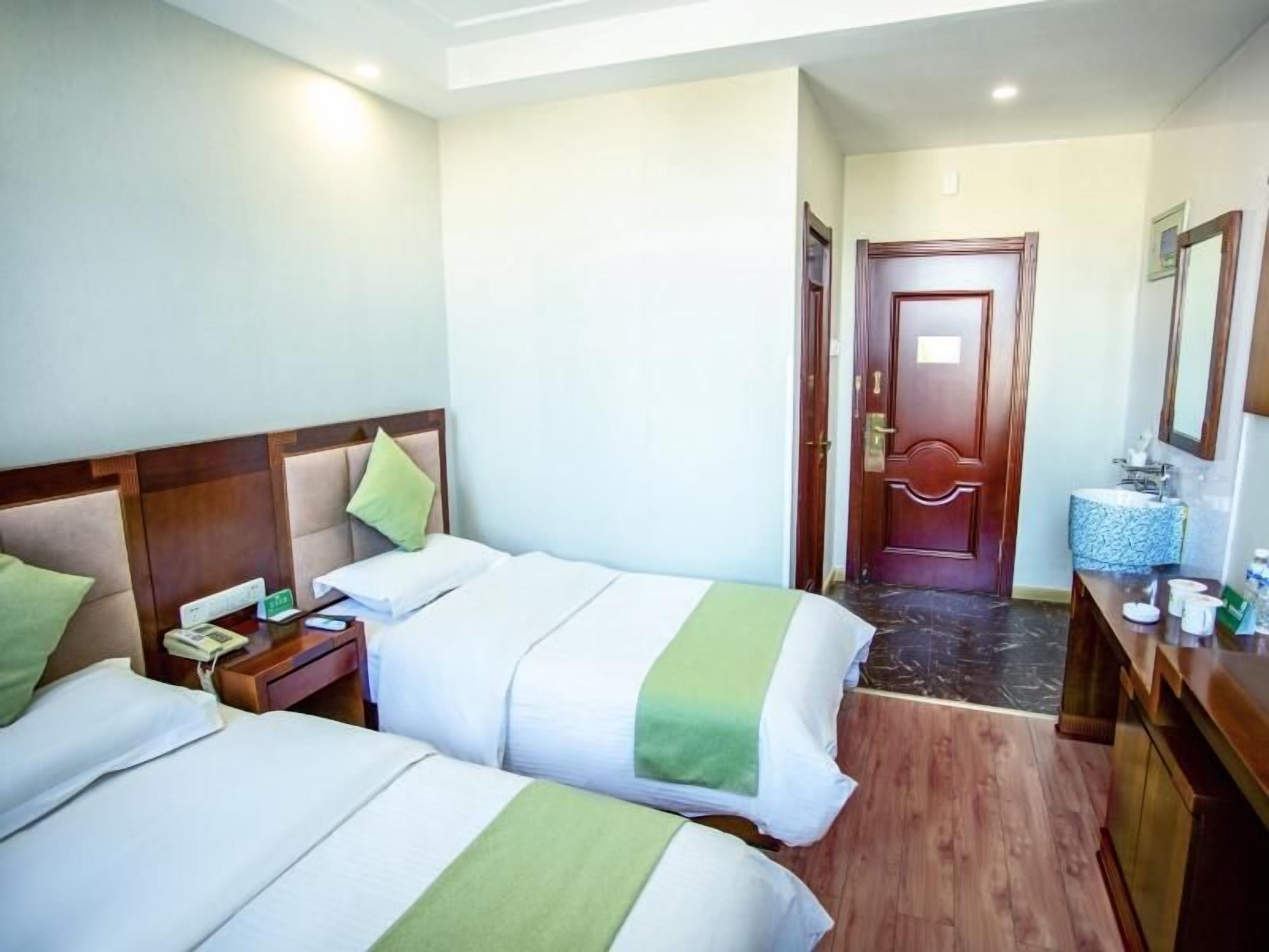 A hotel room with two beds, a wooden headboard, a bedside table with a phone, a mirror, and a door leading to another room.