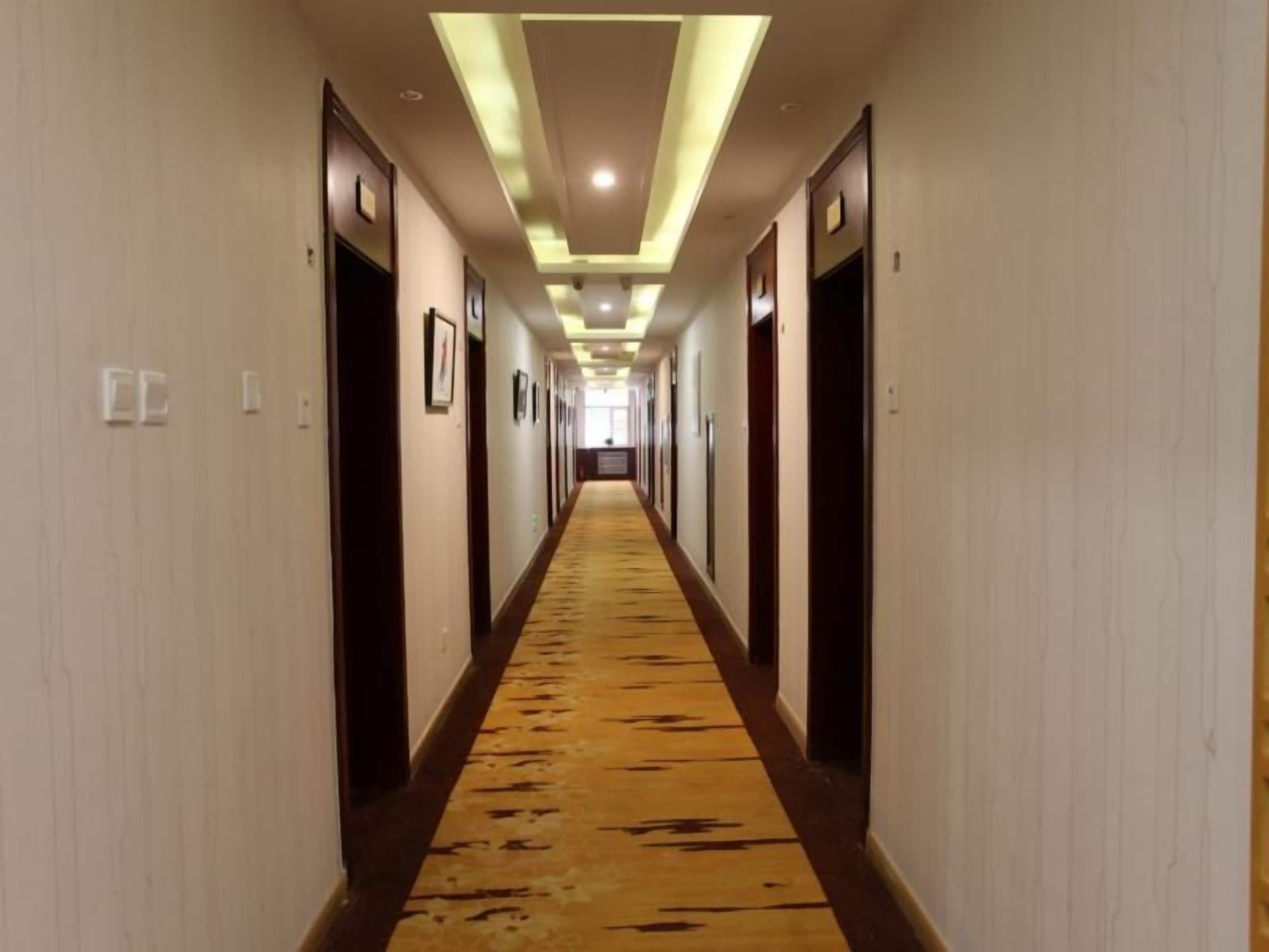 A hotel hallway with doors on both sides, a carpeted floor, and recessed lighting.