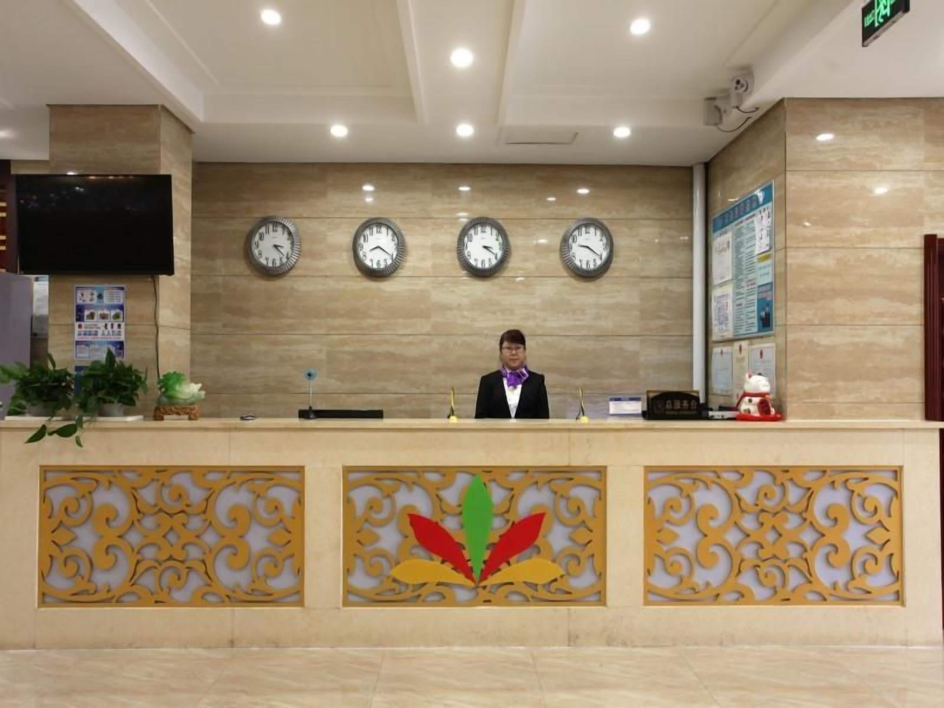 A reception desk with a clock, a flat-screen TV, and a decorative leaf pattern on the wall.