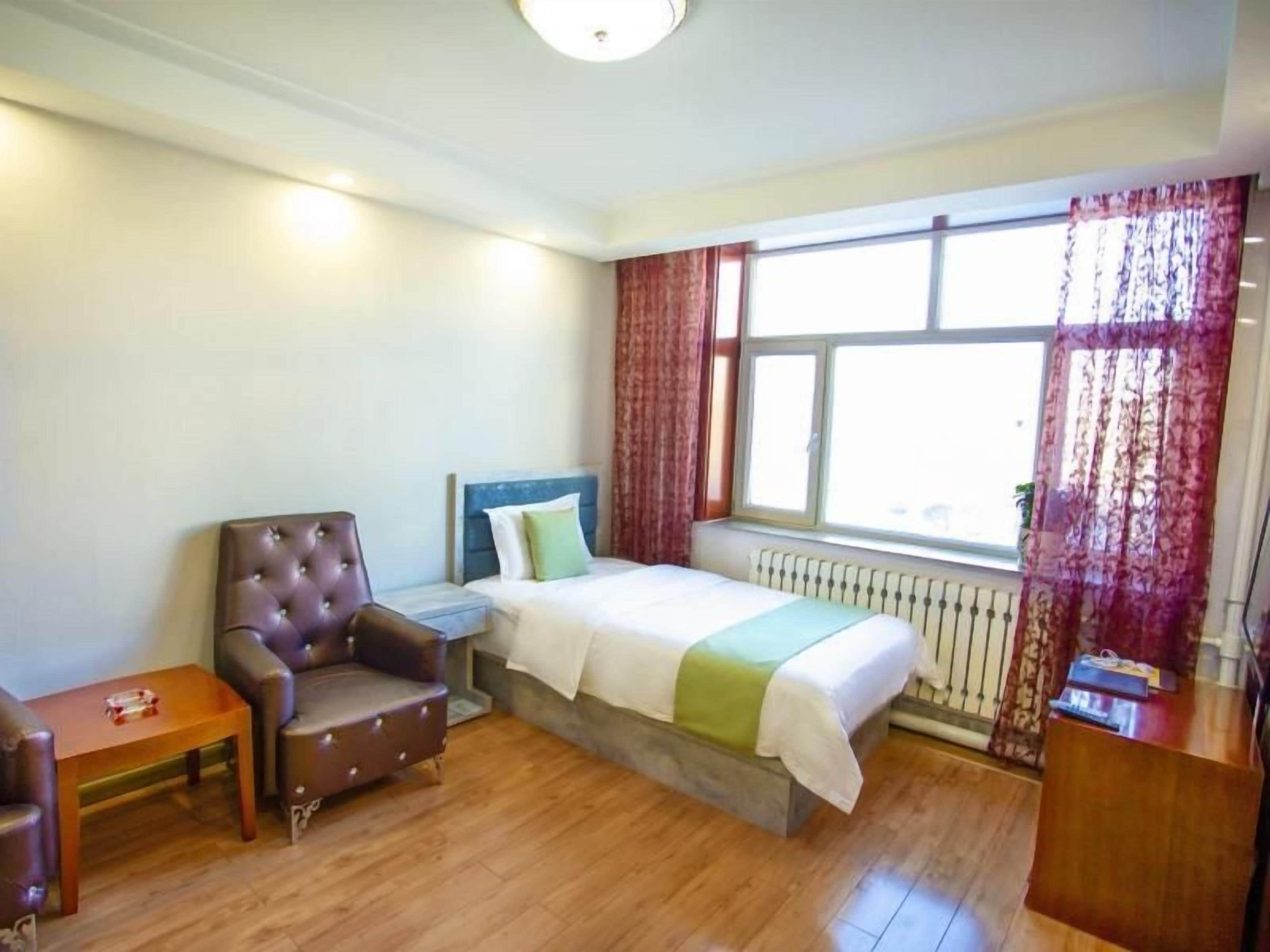 A hotel room with a bed, a chair, a table, and a window with curtains.