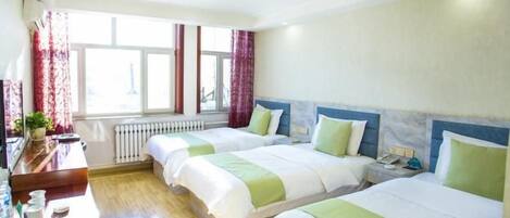 A hotel room with two beds, a wooden desk, a radiator, and a window with curtains.