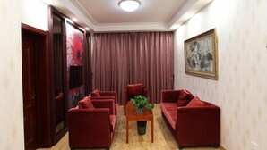 A living room with a wooden floor, red sofas, a coffee table with a plant, a painting on the wall, and a door with a red curtain. - Greentree Alliance Hulunbeier Zhalantun Railway Station Hotel (Hulunbuir)