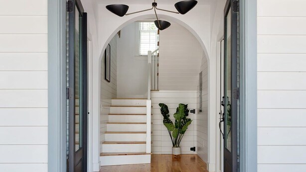 Una entrada moderna con una escalera de madera, un felpudo negro y beige, y un colgador de luz.
