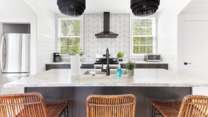 Una cocina moderna con una isla grande, dos lámparas colgantes y un refrigerador de acero inoxidable.
