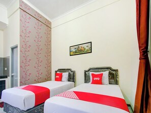 Een hotelkamer met twee bedden, elk voorzien van een rood-witte sprei, een rood kussen met de tekst 'OYO' erop en een ingelijst foto aan de muur.