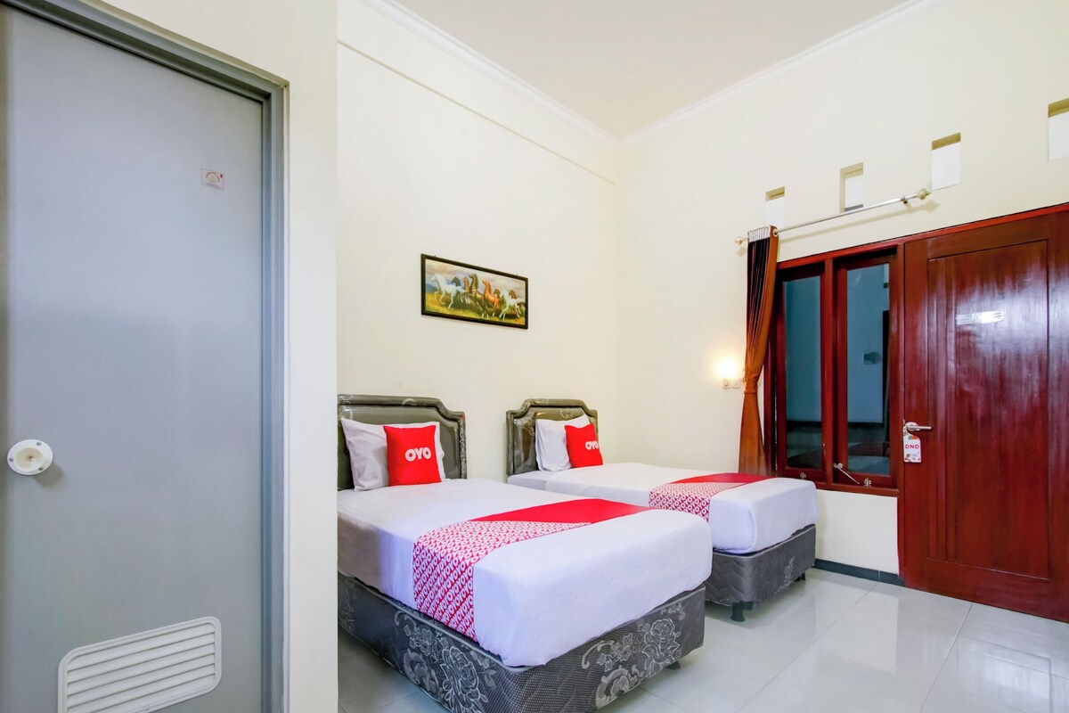 Une chambre d’hôtel avec deux lits, une porte, une fenêtre avec des rideaux et un tableau accroché au mur.
