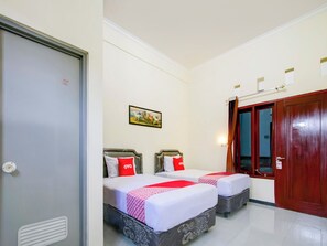 A hotel room with two beds, a door, a window with curtains, and a wall-mounted picture.