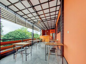 Zona pranzo all'aperto con tavoli e sedie, un bancone in legno e vista sul verde.