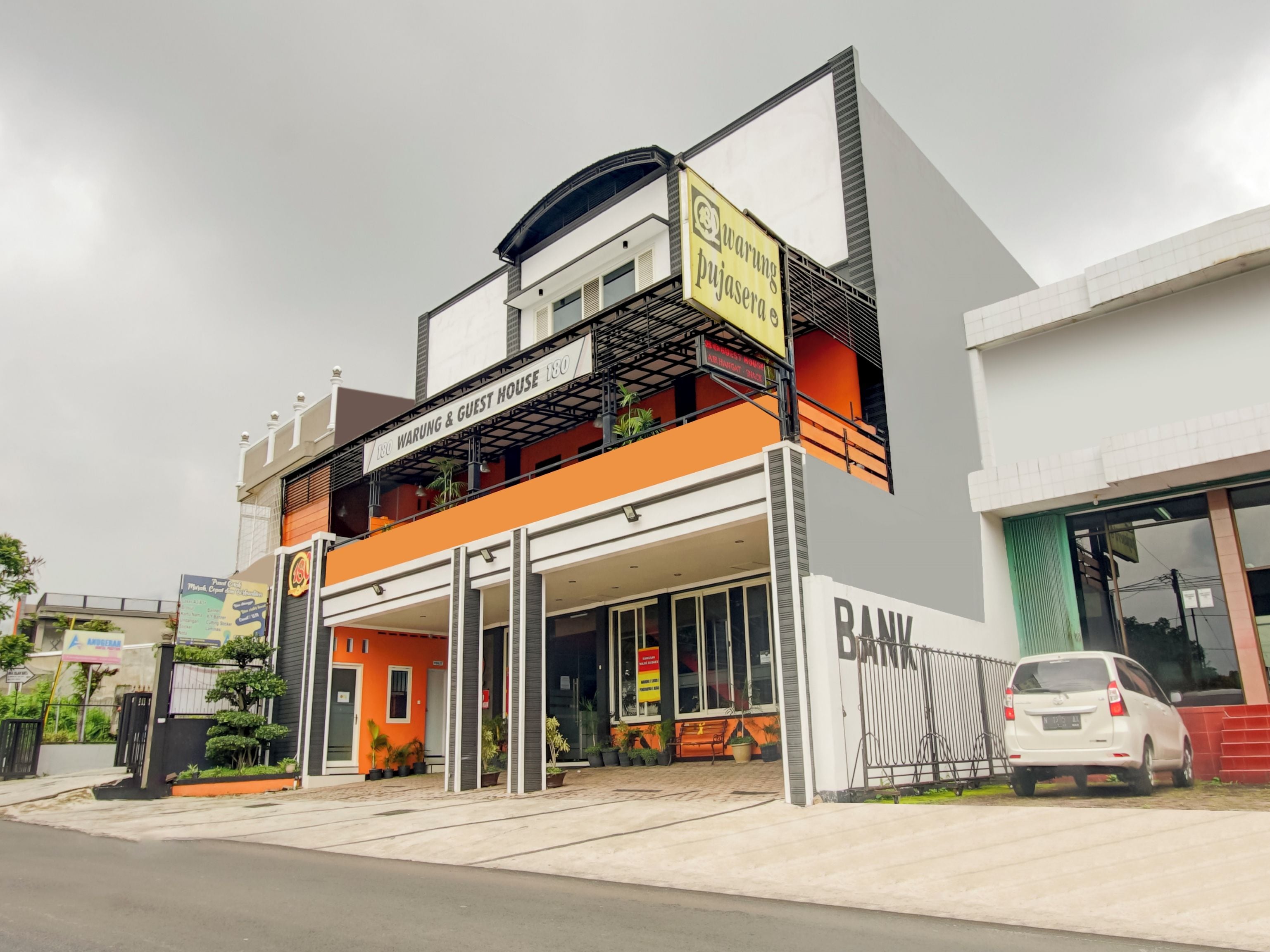 Un edificio de dos pisos con un letrero que dice 'Warung Pujasera' y 'Warung & Guest House' en el nivel superior.