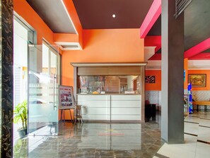 Una hall dell'hotel con una reception, un ingresso con porta in vetro e un pavimento piastrellato.