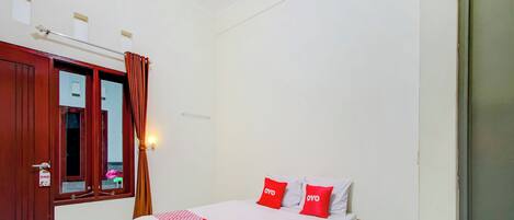 A bedroom with a wooden bed, red and white bedding, a mirror, a door with a sign, and a wall-mounted light fixture.